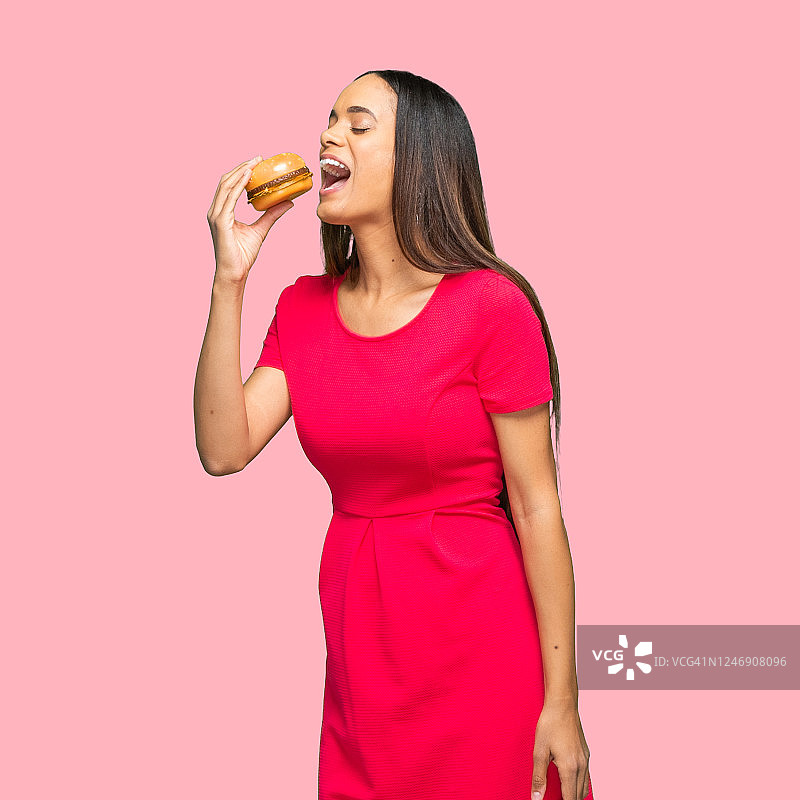非裔美国女性穿着裙子，手拿小面包站在有色背景前图片素材