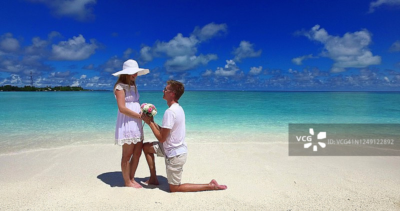 在热带海滩上求婚。那个男人跪在女友面前，向她求婚。幸福的年轻夫妇在生活的下一步图片素材