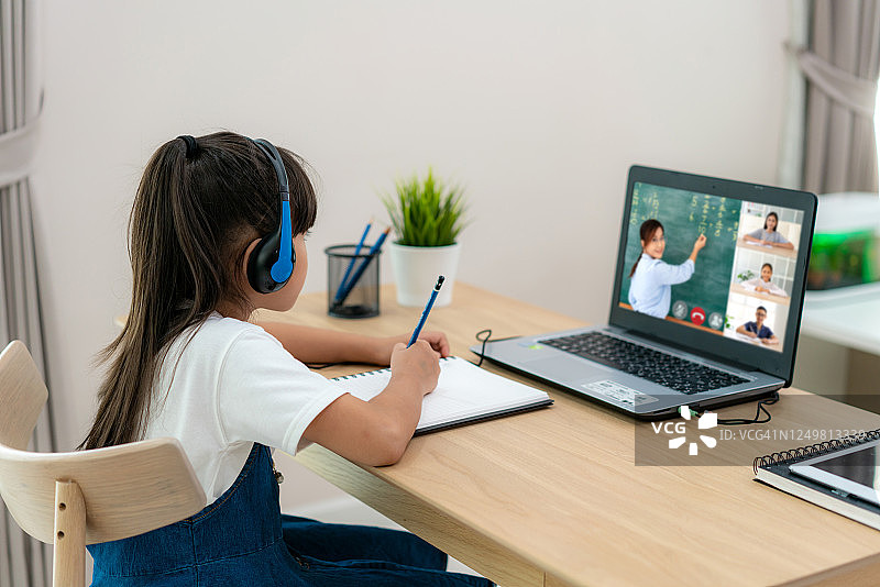亚洲女学生视频会议电子学习与老师和同学在电脑上在家里的客厅。在家教育和远程学习，在线，教育和互联网。图片素材
