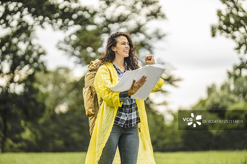 年轻女子穿着防水夹克，看地图，在雨中徒步旅行图片素材