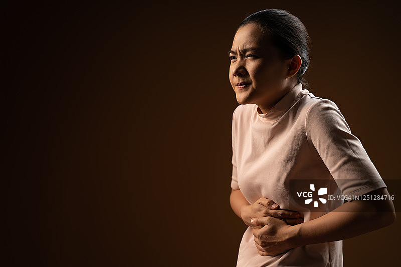一名亚洲女性胃痛，孤立地站在米色背景上。图片素材
