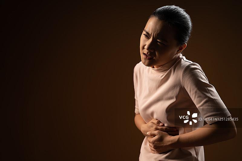 一名亚洲女性胃痛，孤立地站在米色背景上。图片素材