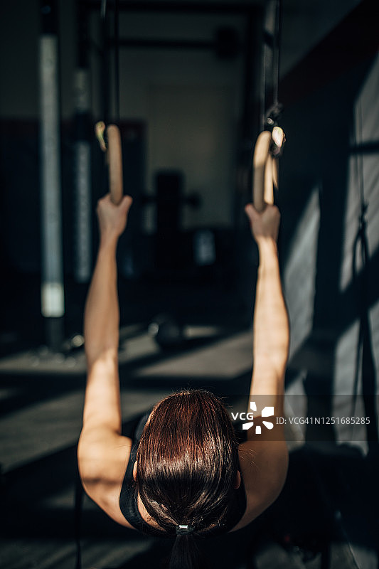 健康的年轻女子在健身房的体操吊环上锻炼图片素材