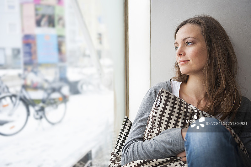 一幅在咖啡店里做白日梦的女人在冬天透过窗户向外看的肖像图片素材