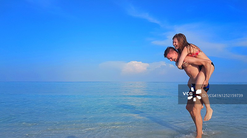 一对幸福的夫妇在海滩上玩，一个女人骑着一个男人回到马尔代夫的岸上图片素材