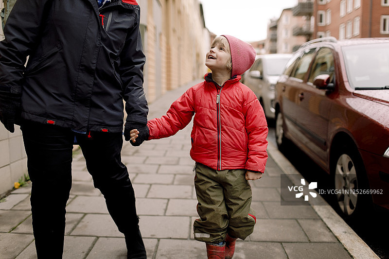 笑眯眯的孙子穿着暖和的衣服，牵着奶奶的手走在人行道上图片素材