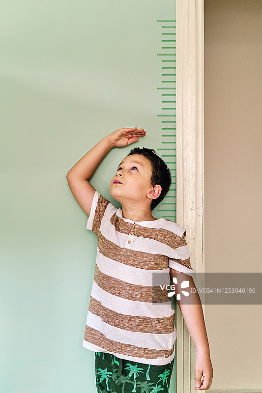 孩子在墙上测量自己的身高。他长得真快。图片素材