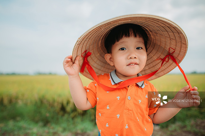 带着传统藤帽的亚洲华人男孩站在稻田边的肖像图片素材