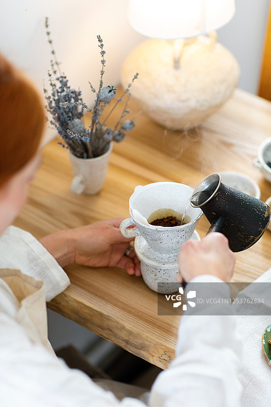 女人用手把热水倒在陶瓷餐具里的过滤咖啡上。早晨例行公事。关闭了。图片素材