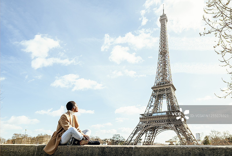 在法国巴黎的一个阳光明媚的日子里，一个年轻的女子看着天空中的埃菲尔铁塔图片素材