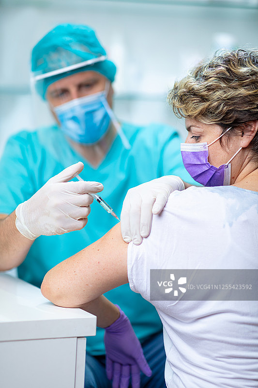 女病人戴口罩，在注射流感疫苗时看自己的手臂图片素材