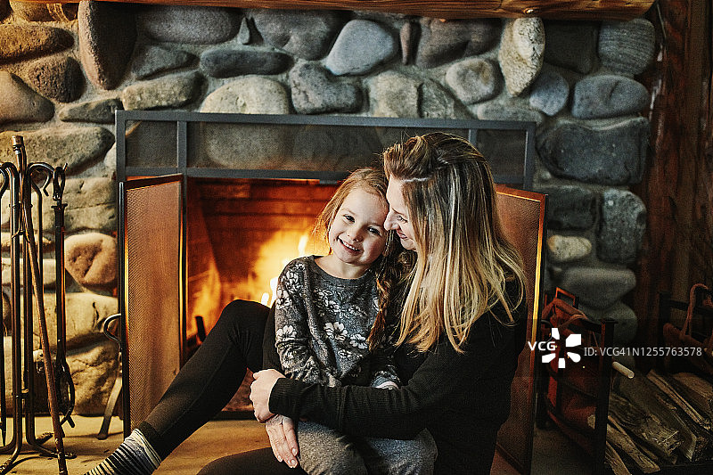 微笑的母亲和女儿一起坐在壁炉前的冬季小屋图片素材