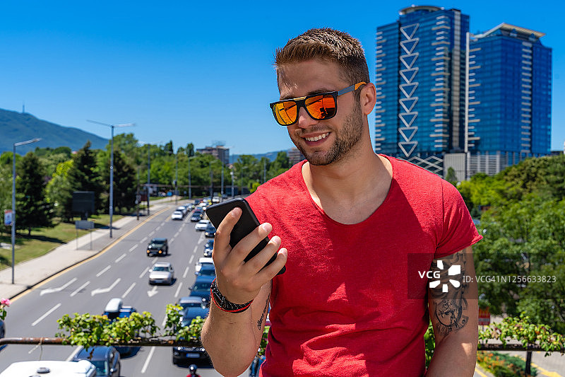 一个年轻人在繁忙的城市街道前拿着智能手机图片素材