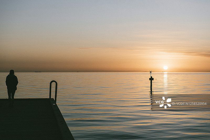 在新冠肺炎疫情限制期间，一个人站在码头尽头，独自看着海面上的日落图片素材