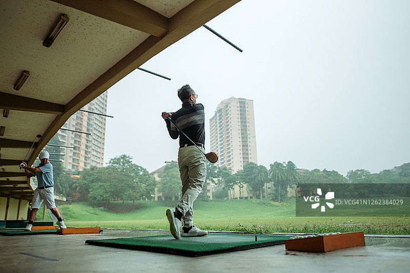 亚洲华人资深高尔夫球手在高尔夫练习场开球并挥杆图片素材