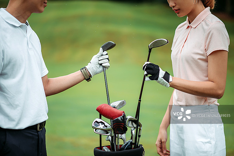 亚洲华人年轻夫妇高尔夫球选手在高尔夫球场上从高尔夫球袋里拿出驾驶俱乐部的Crop shot图片素材