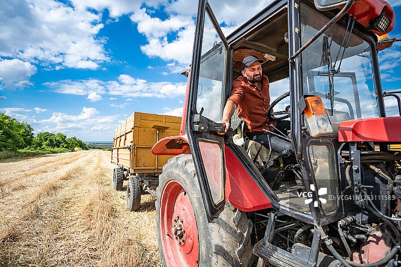 农民驾驶红色拖拉机控制着他的田地里的收成图片素材