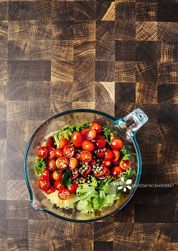 沙拉原料(圣女果，生菜和刺山柑)放在一个碗里，背景是木头图片素材