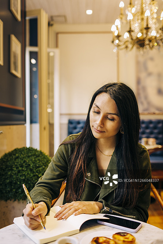 年轻女子坐在咖啡馆里写书图片素材