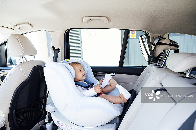 一个男婴坐在车里的儿童座位上，对着镜子看图片素材
