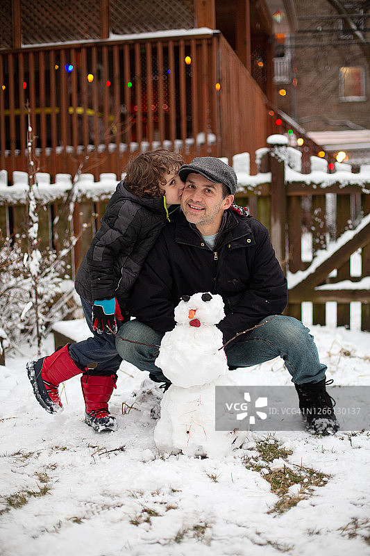 他们在后院堆了一个雪人之后，儿子亲吻他的父亲图片素材