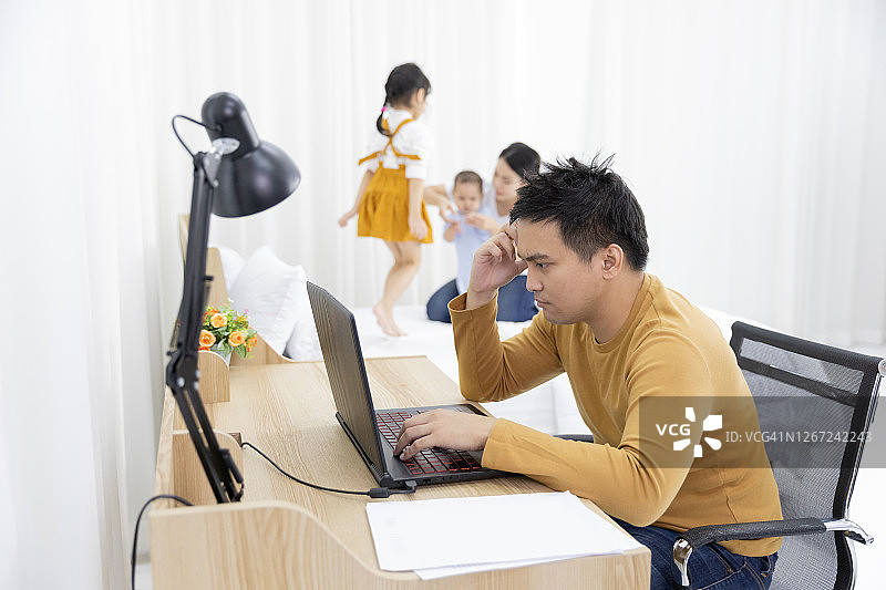 亚洲男性使用笔记本电脑在家工作，压力和家人制造噪音干扰图片素材