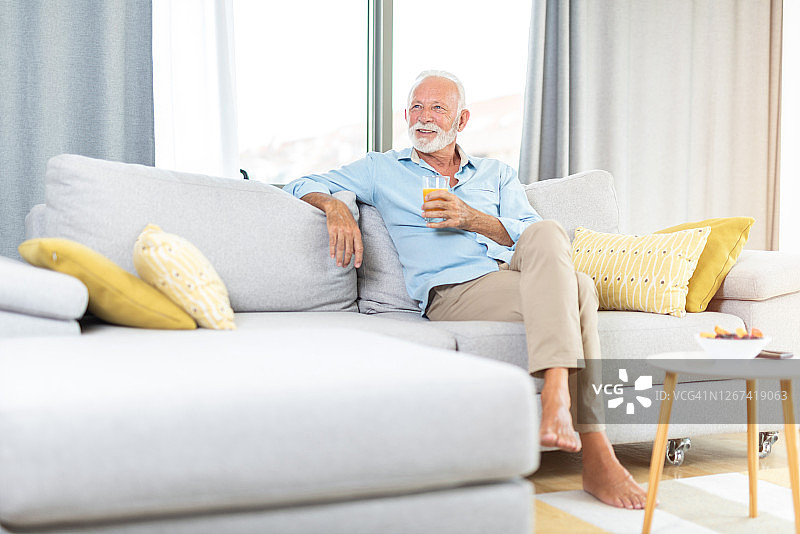 快乐的老人喝着果汁，躺在沙发上休息。图片素材