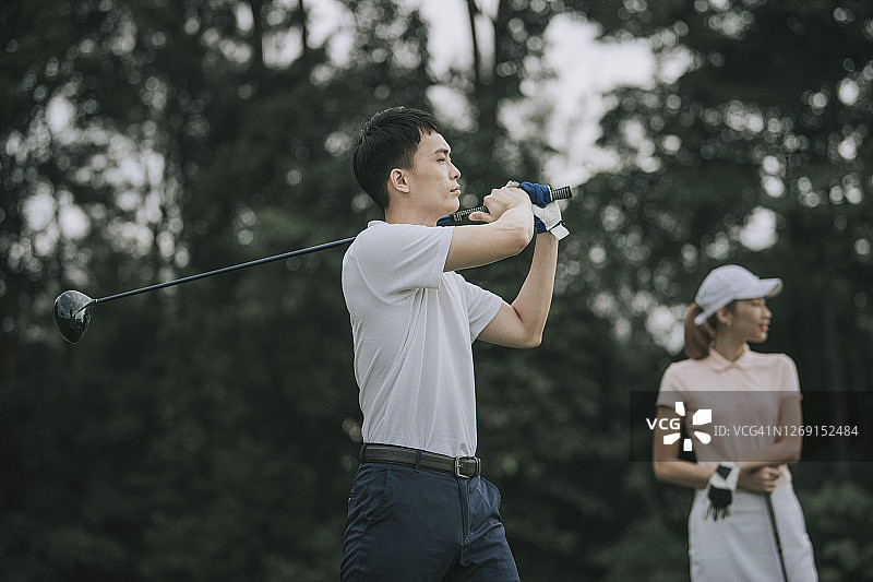 亚洲华人年轻夫妇高尔夫球开球和挥舞他的司机棒在高尔夫球场图片素材