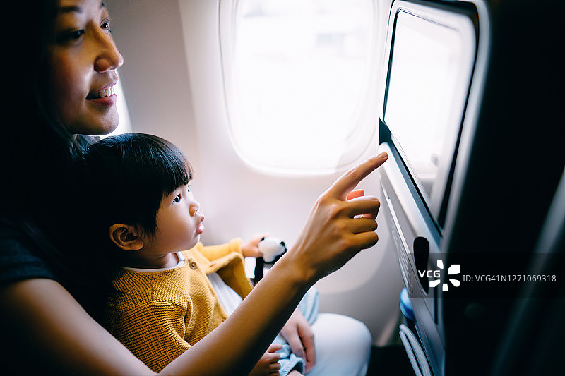 年轻的亚洲母亲和可爱的小女儿一起在视觉屏幕上看卡通，而旅行在飞机上度假图片素材