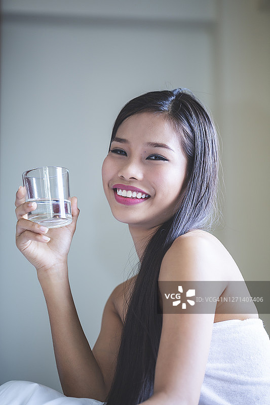 一个年轻美丽的亚洲女人在床上拿着一杯水图片素材