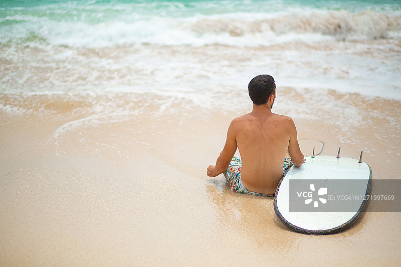 在冲浪后，这家伙正在热带沙滩上休息。健康积极的生活方式在暑假图片素材