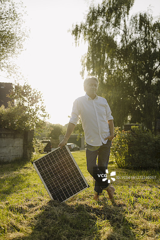 院子里，一名男子手持太阳能电池板，对着晴朗的天空图片素材