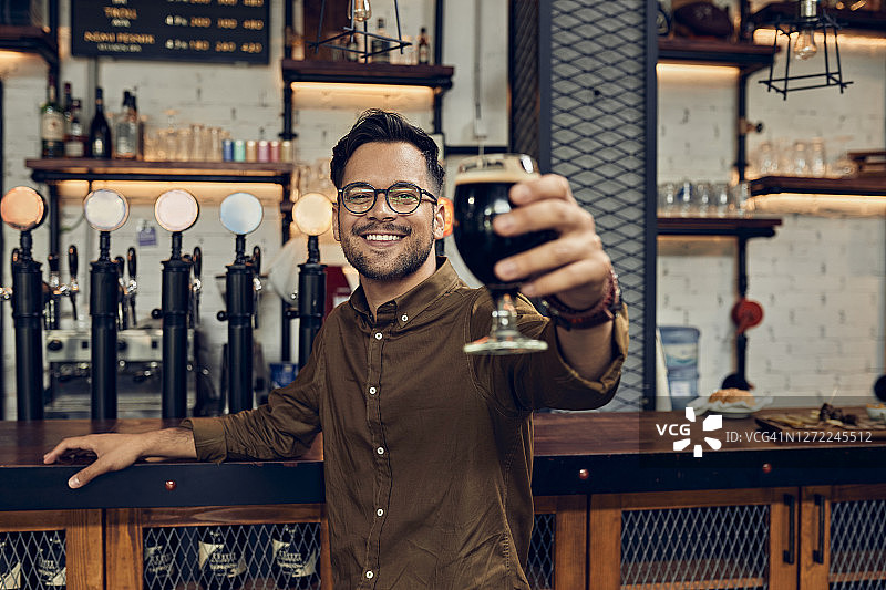 一个微笑的男人在酒吧举起啤酒杯的肖像图片素材