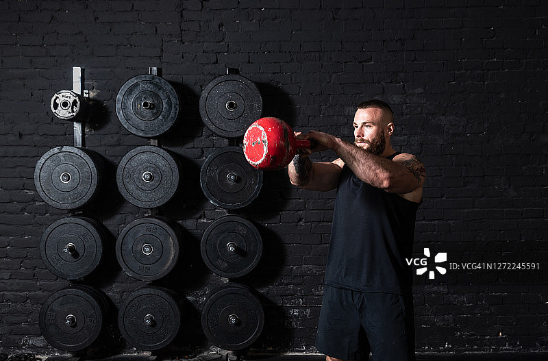 年轻的出汗的肌肉强壮的人与大肌肉做硬核交叉壶铃摆动锻炼训练在健身房图片素材