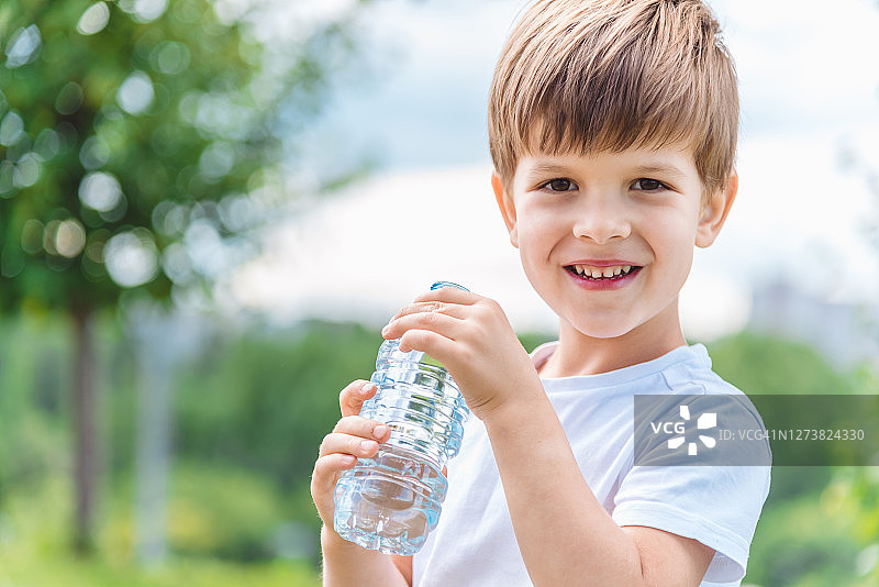 在阳光明媚的日子里，快乐的孩子从瓶子里喝清水图片素材