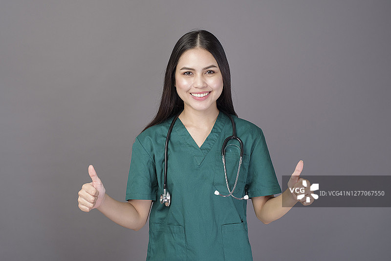 一个女医生穿着绿色的手术服和听诊器在灰色的背景演播室图片素材