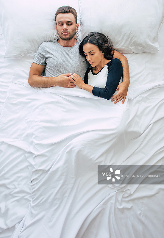 睡觉前。全家人都在睡觉。一对相爱的美丽的年轻夫妇正躺在白色的大床上休息。丈夫和妻子一起在床上。顶视图的照片图片素材