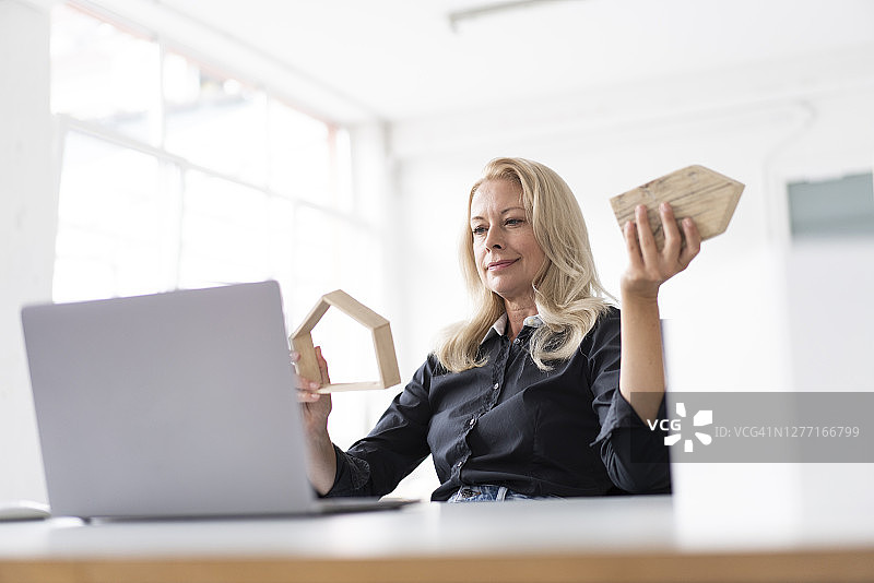 女企业家抱着模型在家，看着桌上的笔记本电脑在家庭办公室图片素材
