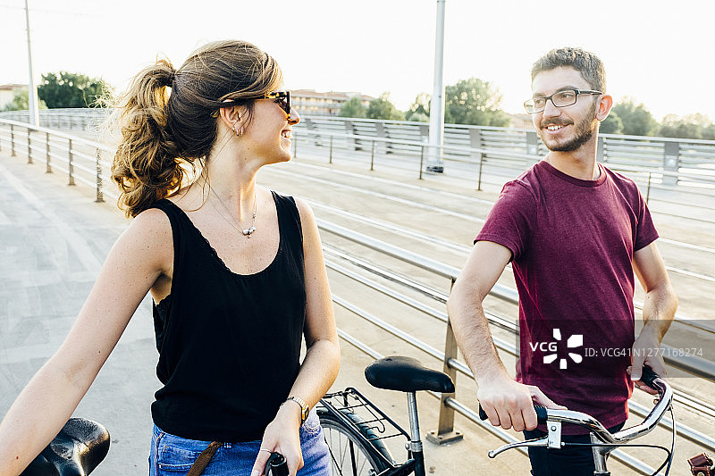 在晴朗的天空下，一对夫妇在桥上骑着自行车聊天图片素材