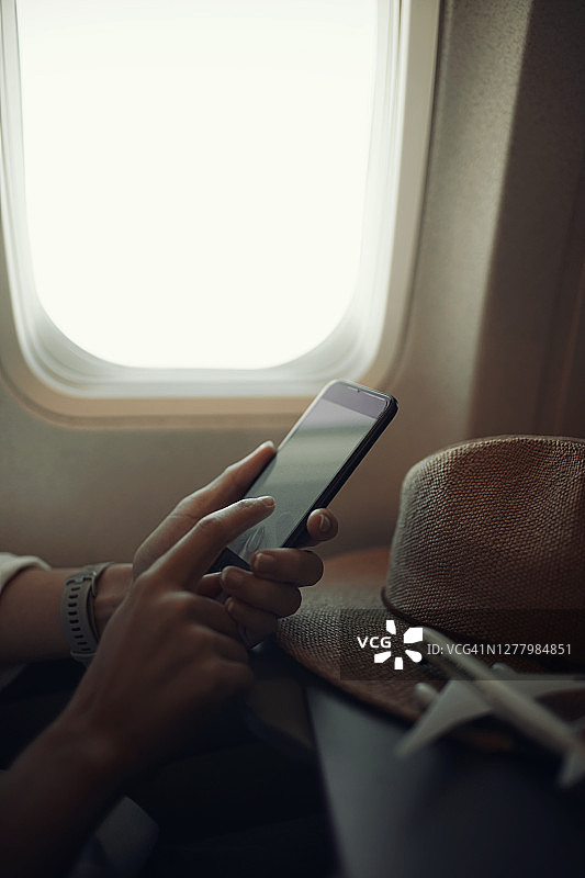 靠近旅客手拿智能手机或手机在飞机靠近窗户的座位图片素材