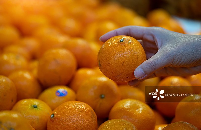男人在超级市场挑选橙子。图片素材