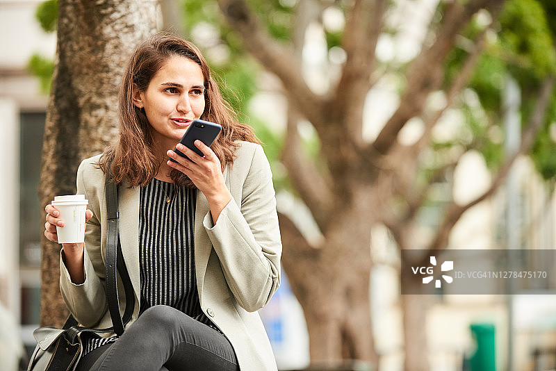 微笑的女人坐在城市的长椅上打电话图片素材
