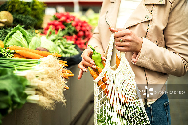 妇女在农贸市场选择绿色植物和蔬菜，并使用可重复使用的环保袋。图片素材