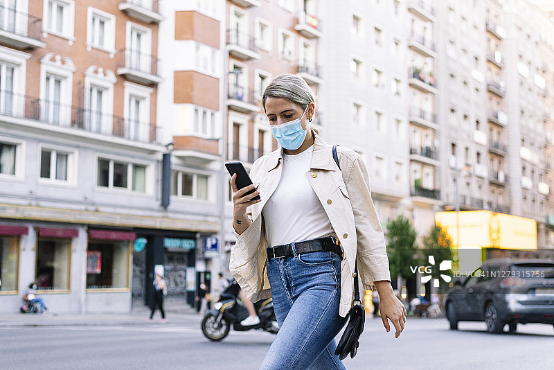 一名年轻女子戴着口罩在城市街道上使用手机图片素材