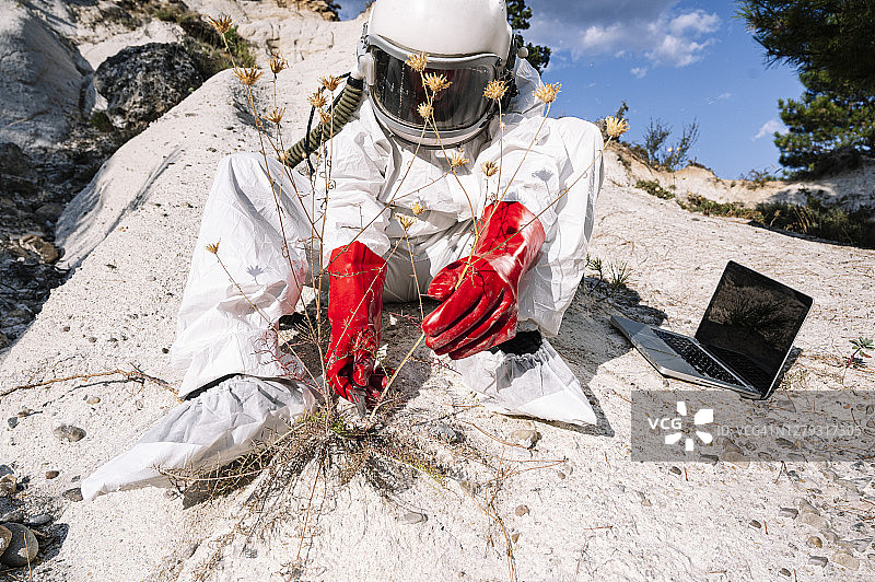 一名男性宇航员在山上拿着笔记本电脑采摘植物图片素材
