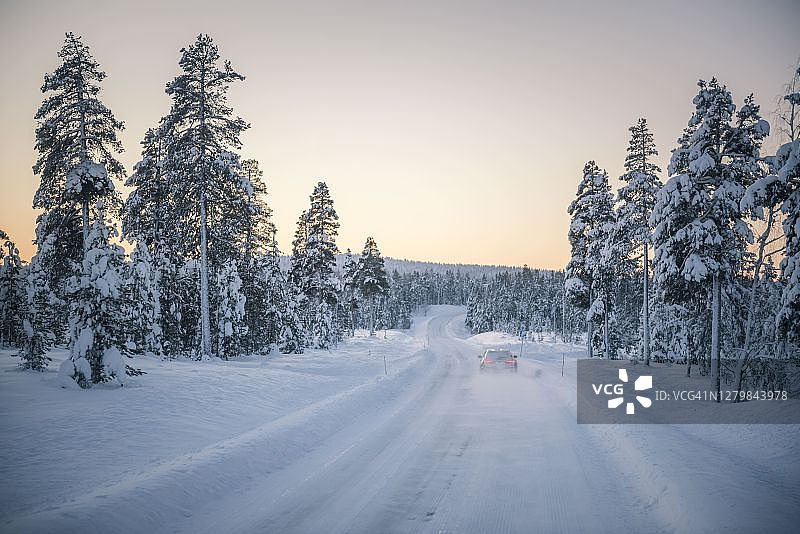 在芬兰北极圈内的拉普兰，一辆汽车在冰雪覆盖的公路上行驶图片素材
