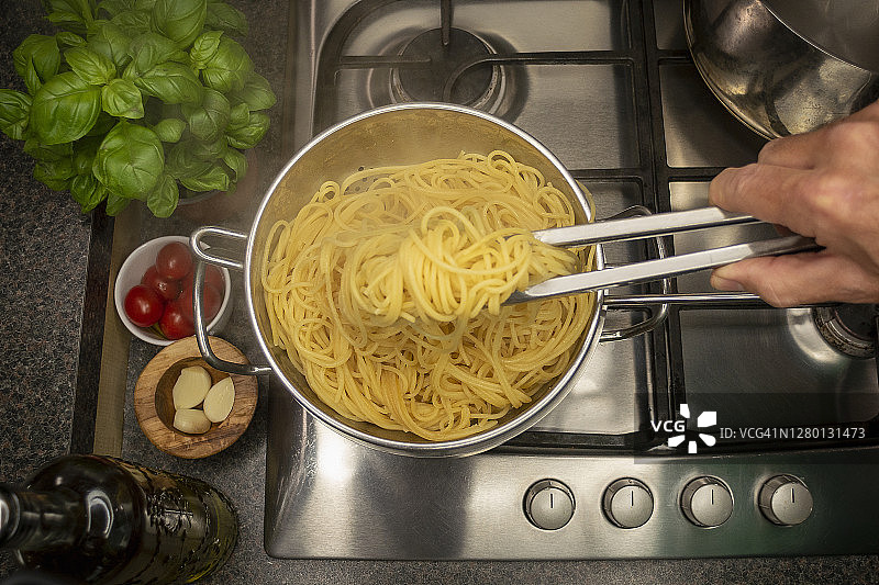 厨房钳子从炖锅里夹上煮好的意大利面。图片素材