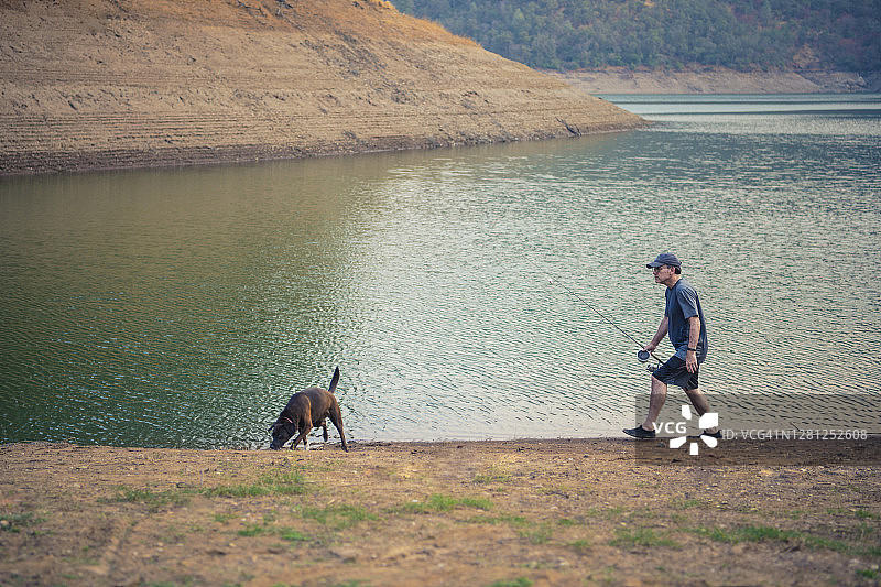 成熟的男人带着钓竿和狗在湖边散步图片素材