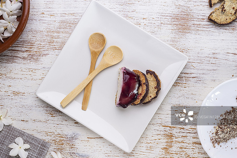 一块芝士蛋糕、蓝莓果酱、燕麦饼干和巧克力放在一个方形盘子里，放在一张风化的白色桌子上图片素材
