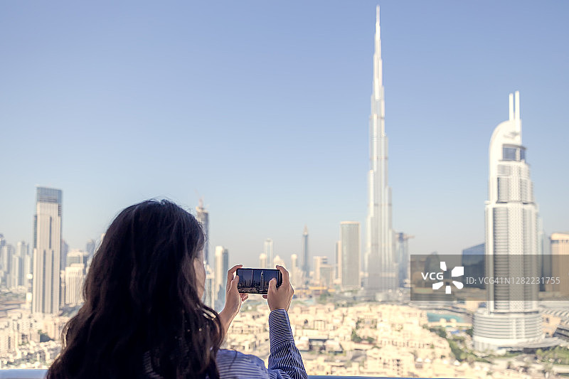 在迪拜摩天大楼阳台上拍照的女人。图片素材